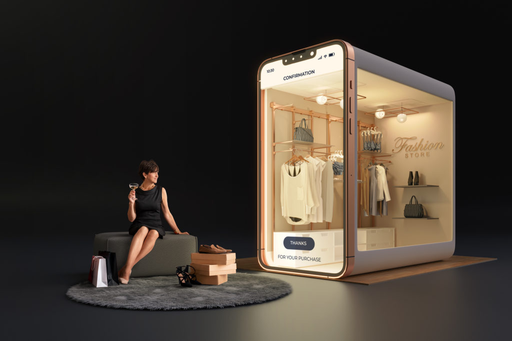 Žena sediaca s pohárom v ruke a dívajúca sa na obchod s oblečením v tvare mobilného telefónu.